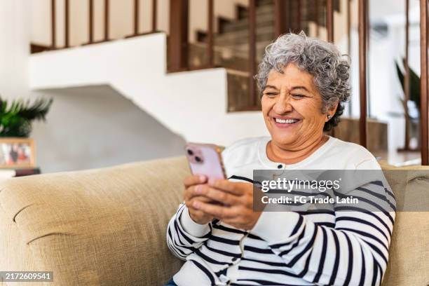 senior woman using mobile phone at home - silver surfer stock pictures, royalty-free photos & images