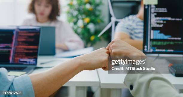 closeup of asian colleagues lgbtqia+ community, share a moment of success with a fist bump, while a focused team works of their sustainable business office. esg sustainable business office. - fist bump stock pictures, royalty-free photos & images