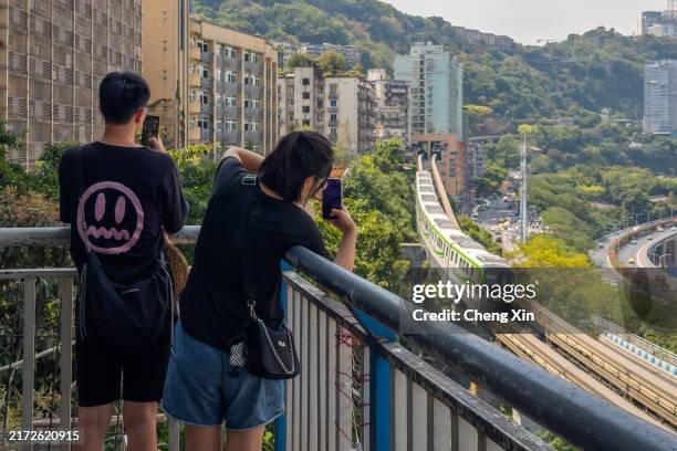 Tourists take photos as a Chongqing Rail Transit train passes through Liziba Station, a popular attraction known for the train traveling through a...