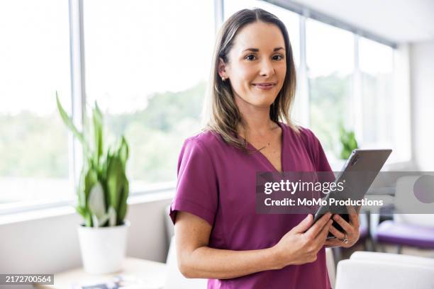 portrait of female nurse in scrubs in doctor's office - vestimenta de hospital fotografías e imágenes de stock