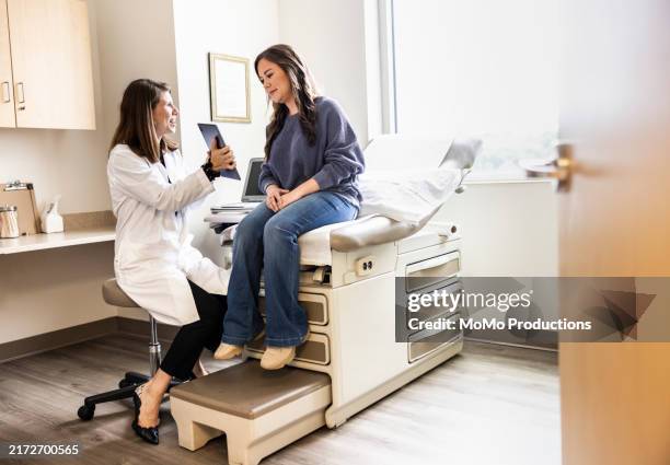 female doctor discussing treatment on digital tablet with female patient in exam room - examination table stock pictures, royalty-free photos & images