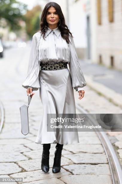 Victoria Barbara is seen wearing black leather heeled boots, silver pendant earrings, a black belt with silver details, a grey handbag, a grey silk...
