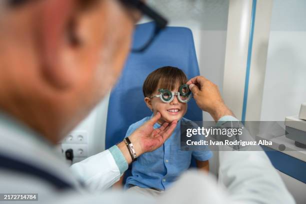 ragazzo sorridente che si fa testare la vista da un optometrista utilizzando un telaio di prova - miopia foto e immagini stock