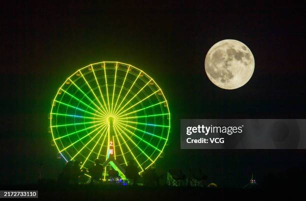 The full moon appears on the night sky over a ferris wheel at a park during Mid-Autumn Festival holiday on September 17, 2024 in Guang'an, Sichuan...