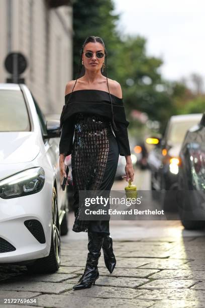 Angela Rozas Saiz wears black sunglasses, gold earrings, shiny sequin black off the shoulder long long sleeve midi dress, shiny black pointed toe...