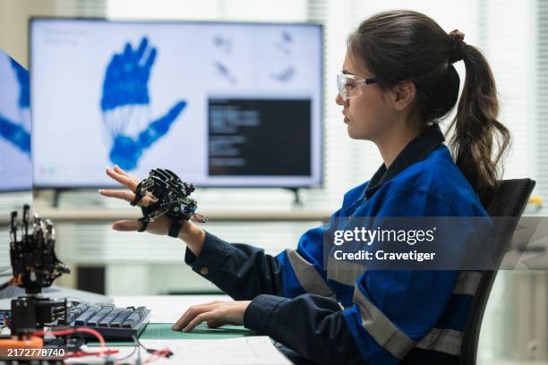 female engineer controls and tests a robotic hand using bluetooth and coding, showcasing expertise in modern robotics and high-tech engineering. - androïde photos et images de collection
