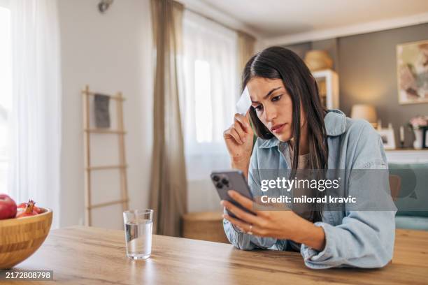 una mujer joven y preocupada que usa su teléfono inteligente para comprar en línea y sostiene una tarjeta de crédito. - preocupado fotografías e imágenes de stock