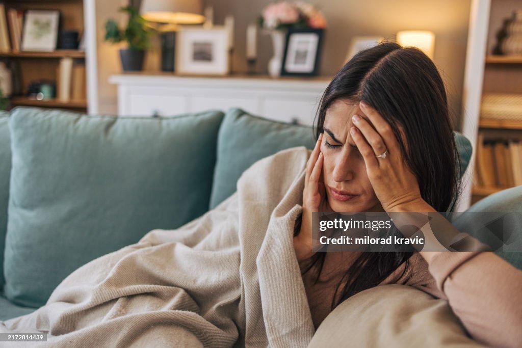 A young woman lying on the sofa in the living room, feeling sick.