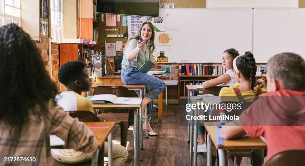 insegnante divertente, felice ed eccitato che parla agli studenti in classe scolastica con un gruppo di bambini che apprendono. donna fiduciosa, amichevole e simpatica che pone domande sull'educazione dei bambini diversi durante la lezione di studio - aula foto e immagini stock