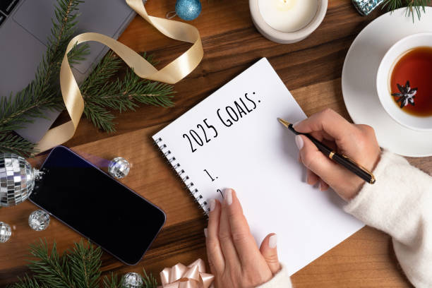 concept of writing the goals on merry christmas and happy new year holidays with woman's hands and notebook with written 2025 year goals on wooden table. - new year resolution stock pictures, royalty-free photos & images