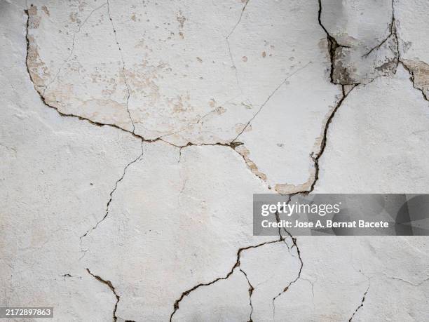 white cement wall with cracks. - gebrochen stock-fotos und bilder