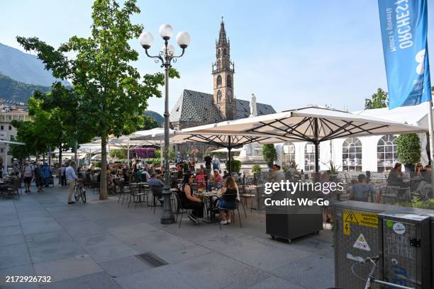 tourists and locals sit in a street café on the walther-von-der-vogelweide square (piazza walther) with the cathedral of the assumption of the virgin mary in the background in the center of bolzano. - bolzano stock pictures, royalty-free photos & images