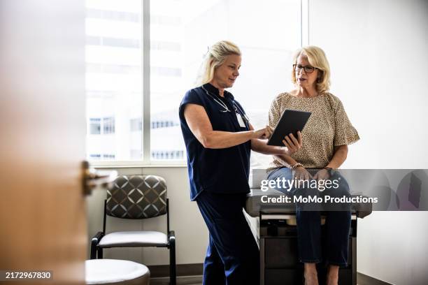 female doctor in scrubs consulting with senior woman in exam room - mesa de examinación fotografías e imágenes de stock