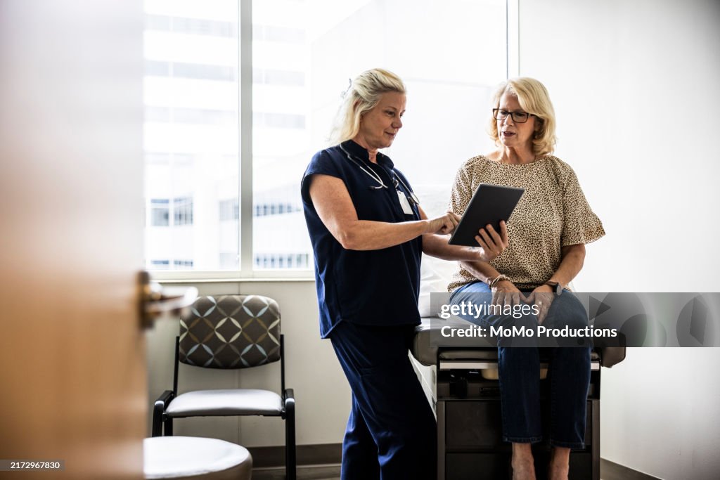 Female doctor in scrubs consulting with senior woman in exam room