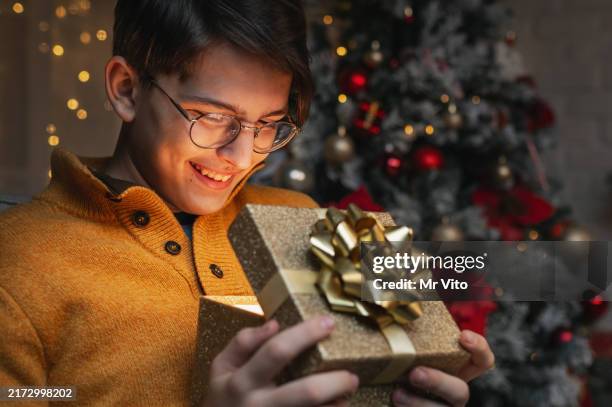 ein teenager öffnet ein geschenk am neujahrsbaum - gift lounge stock-fotos und bilder