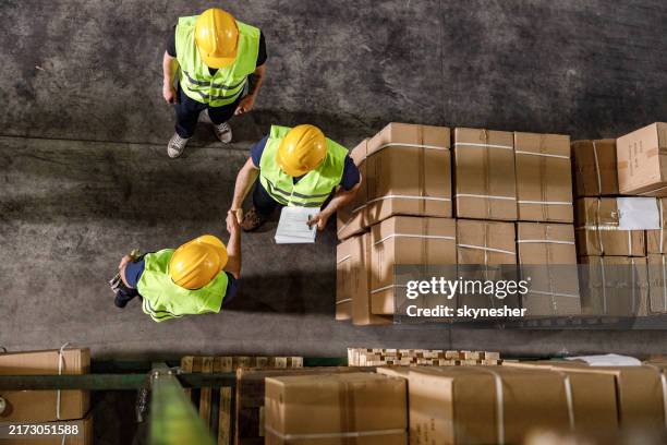 above view of manual workers shaking hands in a warehouse. - casco de trabajo fotografías e imágenes de stock