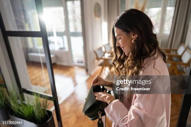 frau arrangiert geldbörse, während sie im flur steht und sich auf das ausgehen vorbereitet - handtasche stock-fotos und bilder