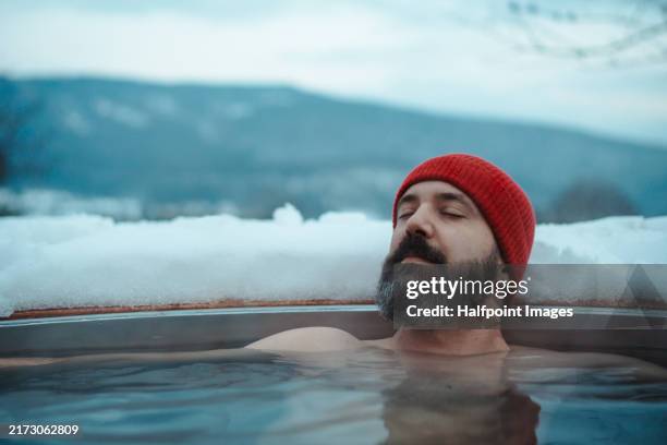 neurodivergent man bathing in wood-burning hot tub, taking moment to relax and regulate in cold weather. hygge winter, peaceful, cozy moments for yourself, alone in cabin. - hygge stockfoto's en -beelden