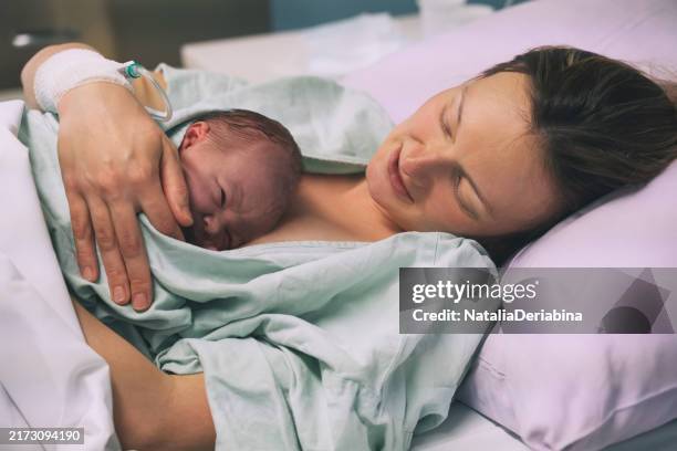 Mother and newborn. Child birth in maternity hospital. Young mom hugging her newborn baby after delivery. Woman giving birth.