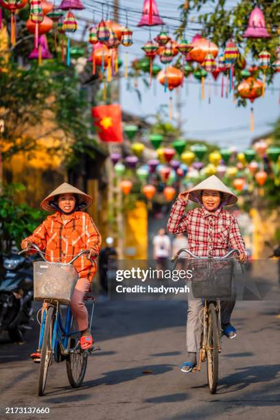 vietnamese women ride bikes in an old town of hoi an city, vietnam - hoi an stockfoto's en -beelden