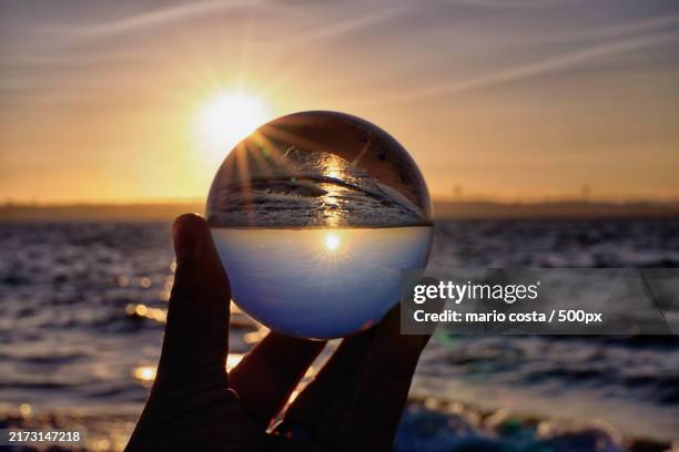 cropped hand holding crystal ball at beach during sunset - glazen bol stockfoto's en -beelden