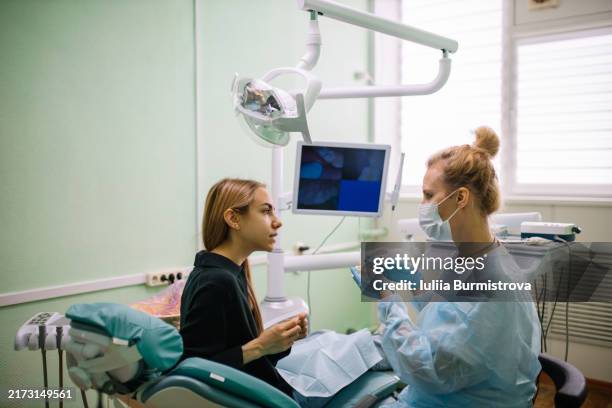 compassionate female dentist in protective workwear and charming young patient engage in discussion using model of human teeth and jaw - molde dental fotografías e imágenes de stock