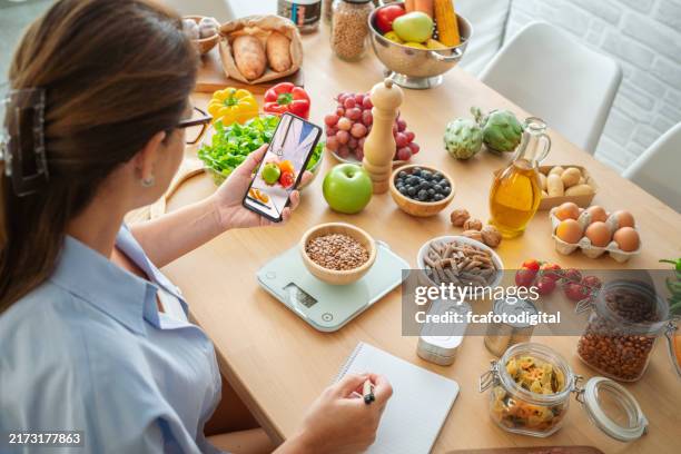 mujer investigando recetas en el celular y tomando notas para planificar una dieta bien balanceada - carbohidrato fotografías e imágenes de stock