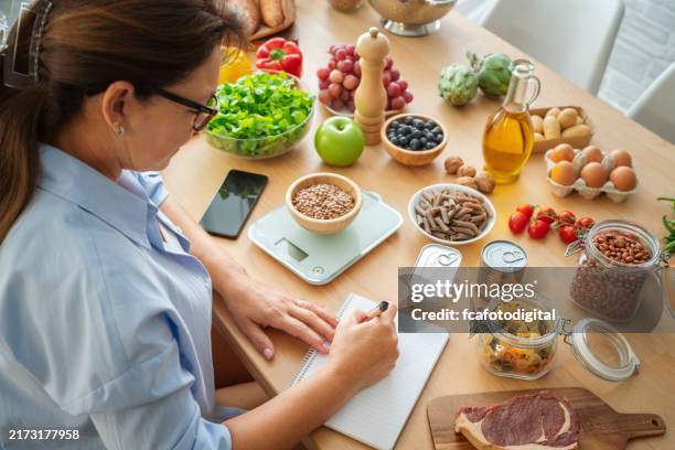 mujer planeando, escribiendo comidas semanales en un bloc de notas del planificador de comidas - carbohidrato fotografías e imágenes de stock