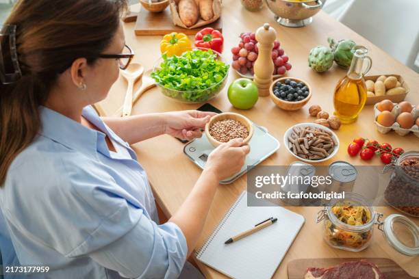 woman using weight scale to measuring proper serving portion of food - serving size stock pictures, royalty-free photos & images
