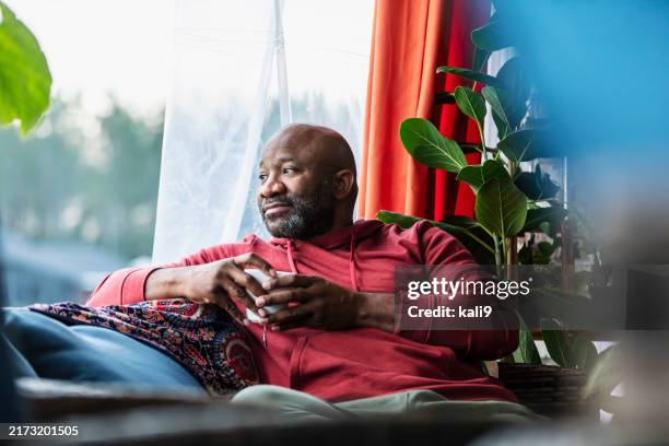 mature multiracial man relaxing at home, drinking tea - zwart etniciteit stockfoto's en -beelden