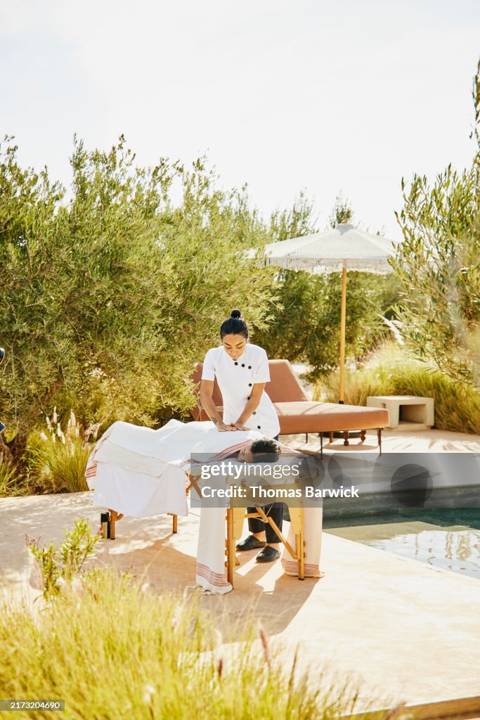 Wide shot guest receiving poolside massage at tropical luxury resort