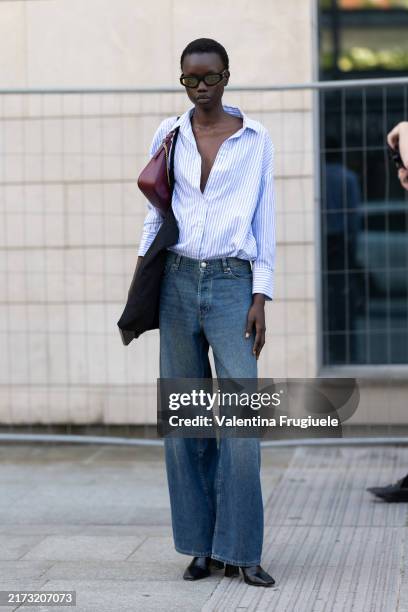 Guest wears black sunglasses, a burgundy leather bag, a light blue and white striped shirt, high waist wide leg jeans and black leather heeled ankle...