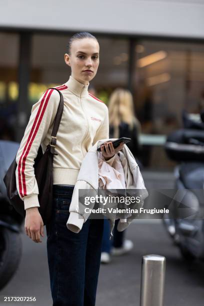 Guest wears a beige and red sweater, a brown bag and blue jeans outside Philosophy show during the Milan Fashion Week Menswear Spring/Summer 2025 on...