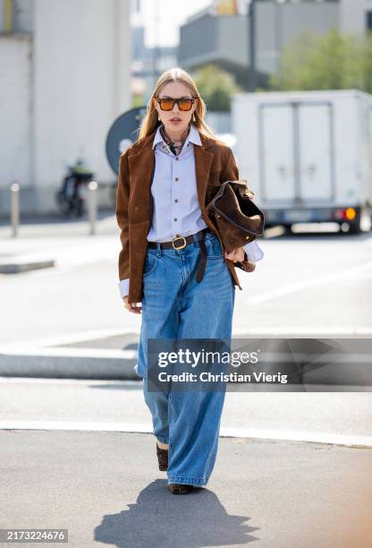 Guest wears denim wide leg jeans, brown jacket, bag, blue button shirt outside Prada during the Milan Fashion Week Menswear Spring/Summer 2025 on...
