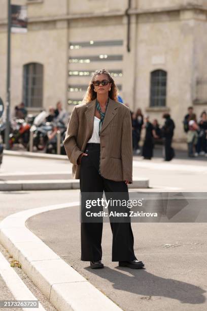 Guest wearing an oversized brown checkered blazer with wide-legged black trousers and sunglasses is seen outside the Prada show during the Milan...