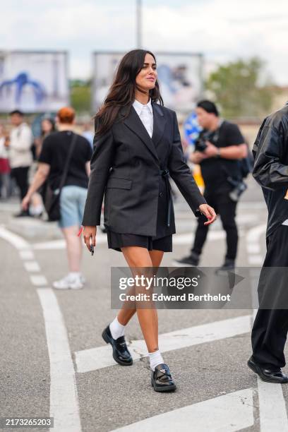 Guest wears white buttoned up long sleeve shirt, black blazer jacket, black mini shorts, white socks, shiny black loafer moccasin leather shoes ,...