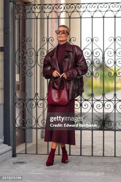Guest wears dark brown sunglasses, gold earrings, dark red Max Mara midi sweater midi dress, dark red oversized leather jacket, shiny dark red Gucci...