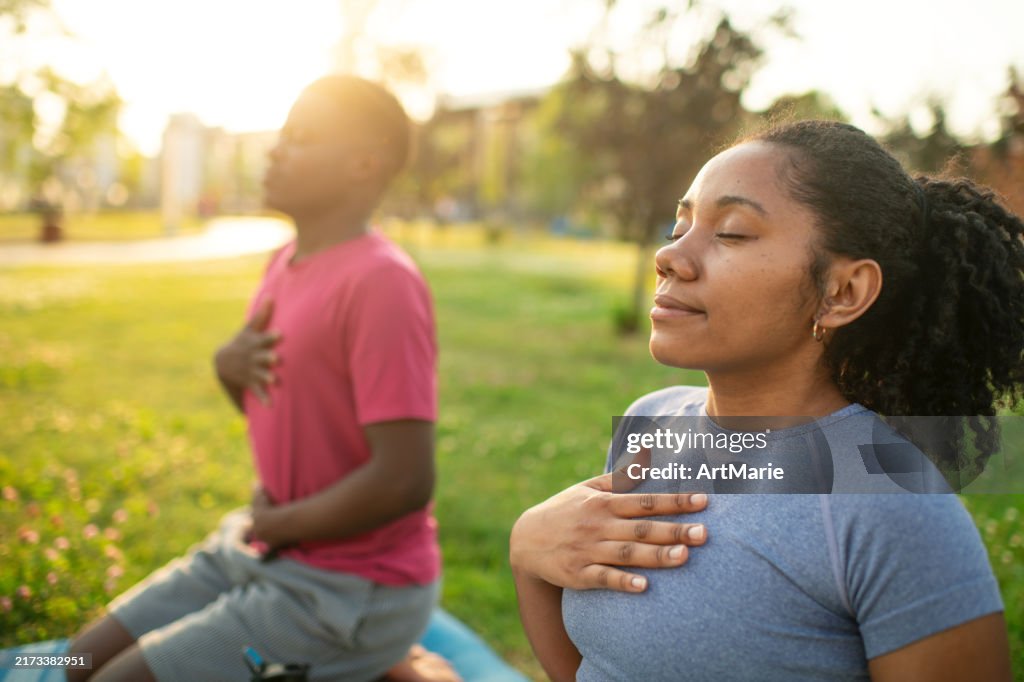 Young couple practicing yoga in a summer park, doing breathing exercise