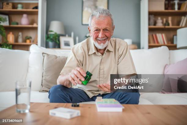 porträt eines lächelnden älteren mannes, der direkt in die kamera schaut, während er medikamente in einer plastikapotheke arrangiert - tablettenbehälter stock-fotos und bilder