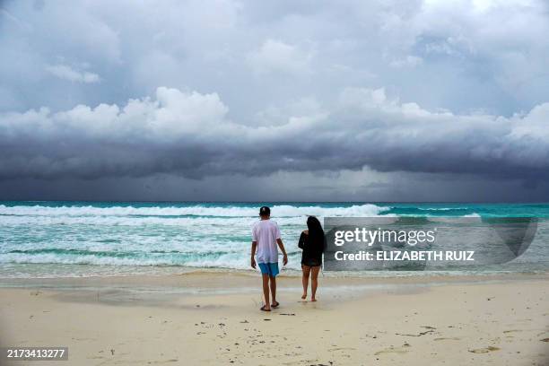 Storm clouds are pictured as a couple walks on the beach ahead of the arrival of tropical storm Helene in Cancun, Quintana Roo state, Mexico on...