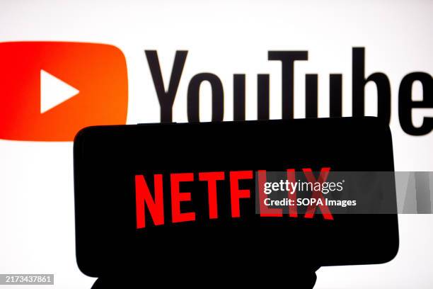 In this photo illustration, a Netflix logo seen displayed on a smartphone with a YouTube logo in the background.