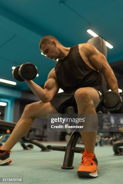 young handsome man exercising with dumbbells in the gym - human muscle stock pictures, royalty-free photos & images