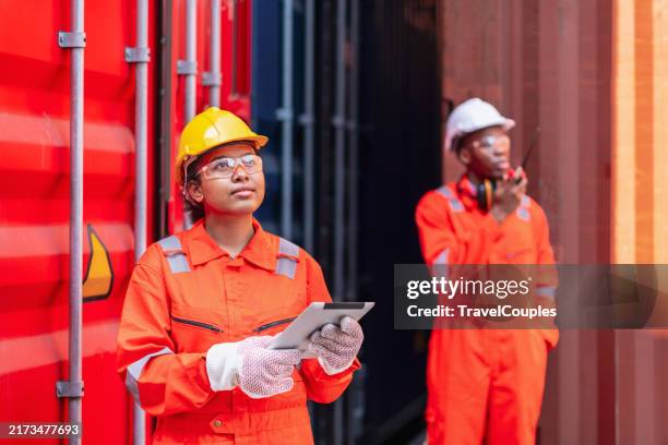confident engineer and tablet at containers yard from cargo freight ship for import export. dock control worker wearing protective coveralls against stack of a containers terminal. colleagues talk about logistics operations. import and export concept - dock worker stock pictures, royalty-free photos & images