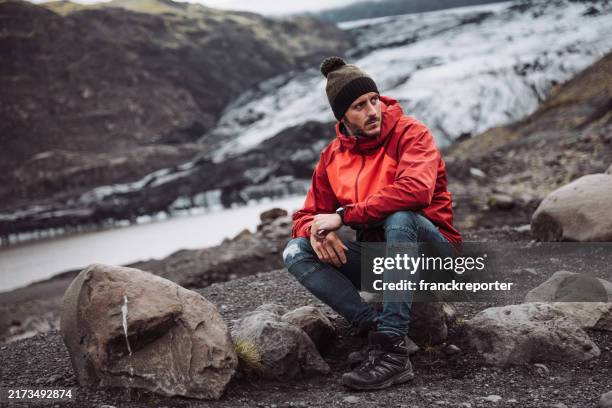 mann sitzt auf einem gletscher in island - regenmantel stock-fotos und bilder