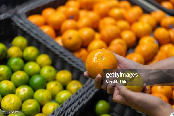 hands holding orange and lime in grocery store - produce aisle stock pictures, royalty-free photos & images
