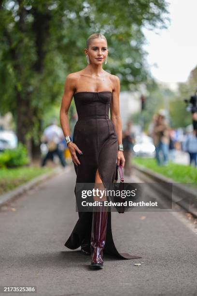Caroline Daur wears silver earrings, dark brown corset Gucci maxi dress with high slits, silver Tiffany & Co, shiny dark red heeled leather boots,...