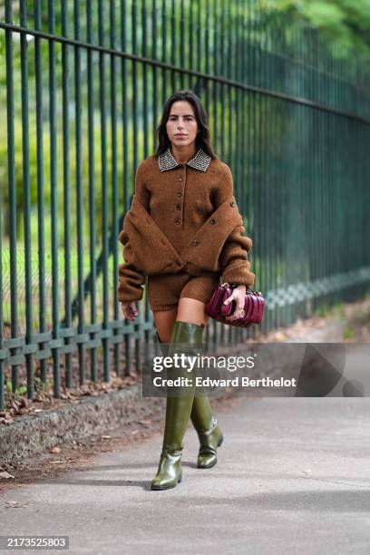 Nina Urgell Cloquell wears dark brown fuzzy long sleeve sweater, dark brown oversized jacket, shiny dark brown fuzzy mini shorts, shiny dark green...