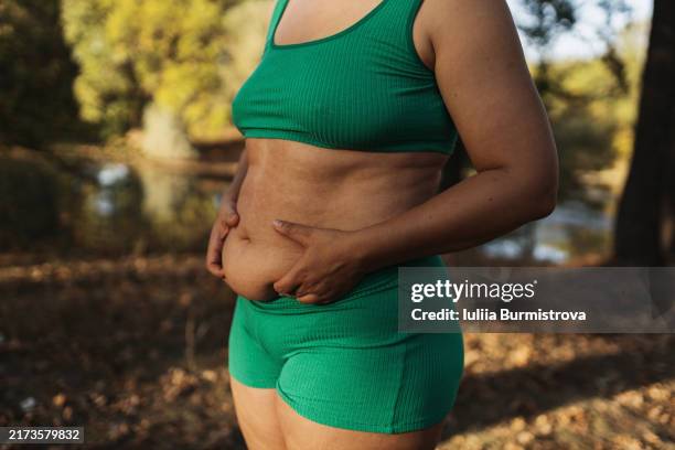 unrecognizable full-bodied woman stands on riverbank and demonstrates exposed body as testament to commitment to healthier lifestyle - menselijke buik stockfoto's en -beelden