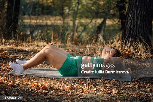 Determined plus-size woman in vibrant green workout ensemble engages in series of crunches on exercise mat by riverside Determined plus-size woman in vibrant green workout ensemble engages in series of crunches on exercise mat by riverside