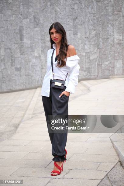 Guest wears a white shirt and black baggy trousers with stripes with red, strapped heels from Armani during the Milan Fashion Week Menswear...